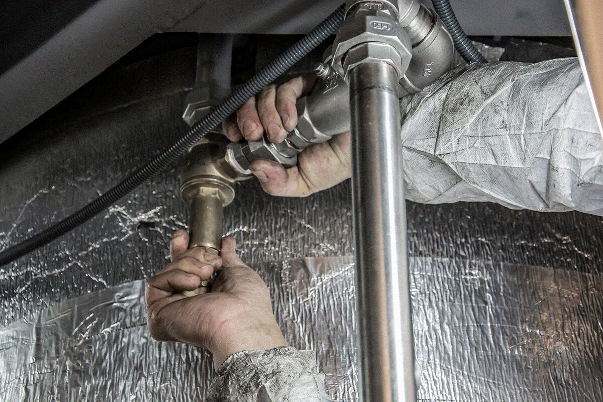 Close-up of hands working on a threaded supply line connection, the kind of joint that fails and floods a property