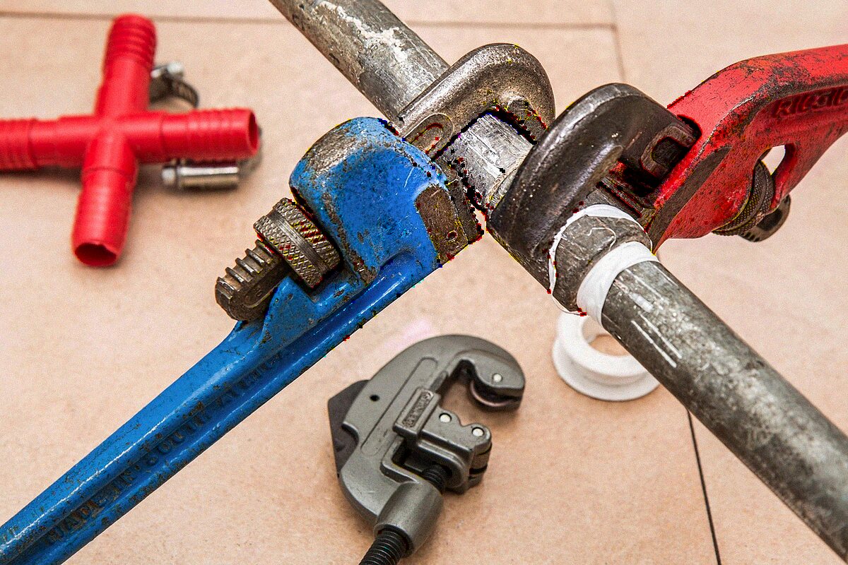 Pipe wrenches, a tube cutter and copper fittings laid out for a supply line repair