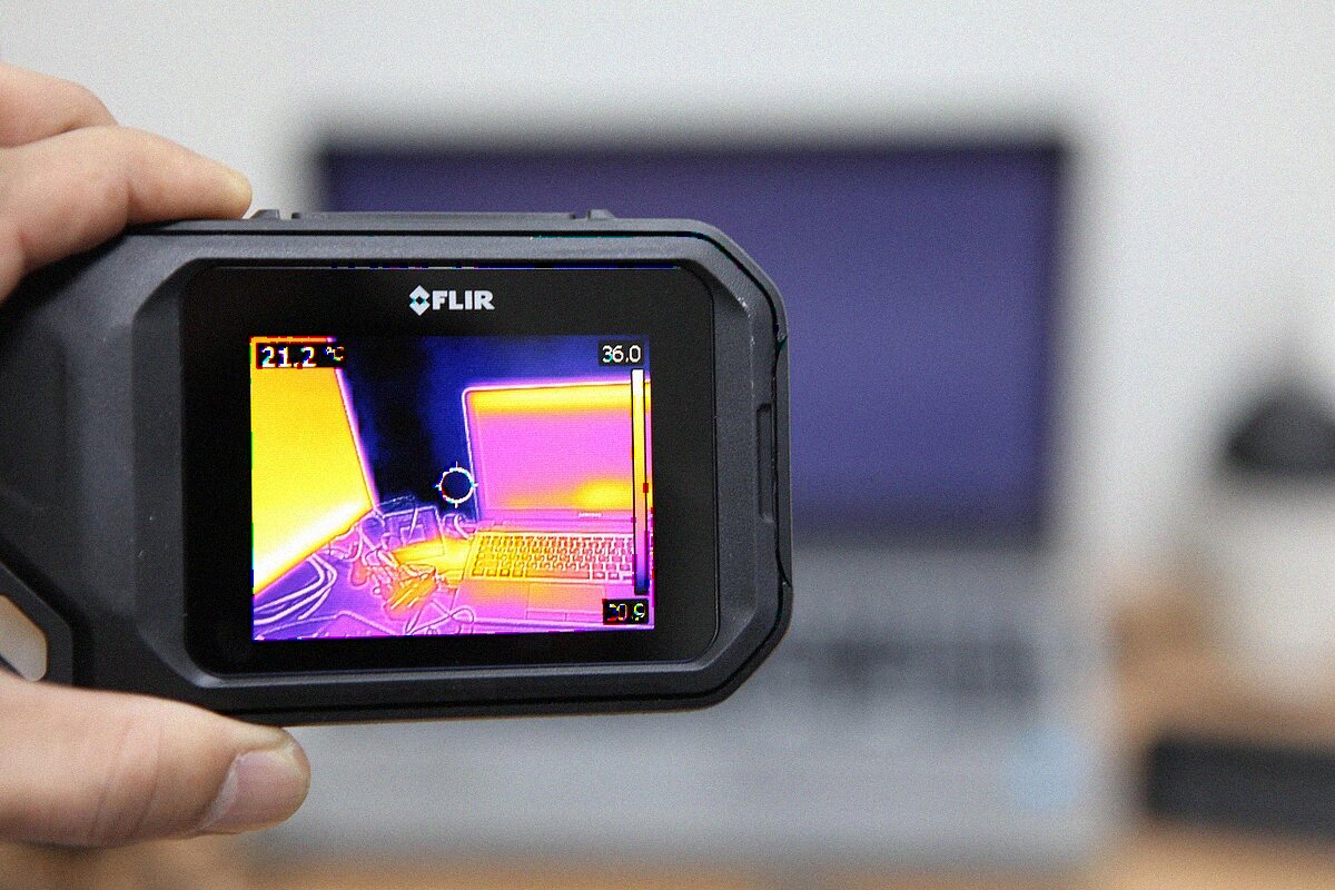 A hand-held thermal imaging camera displaying a heat map of a surface